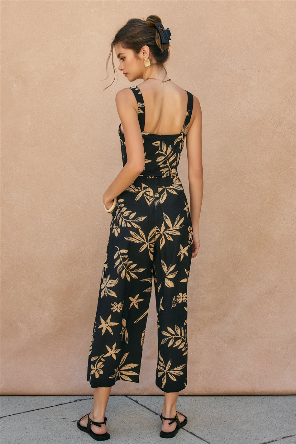 Woman wearing a black floral jumpsuit against a beige wall.