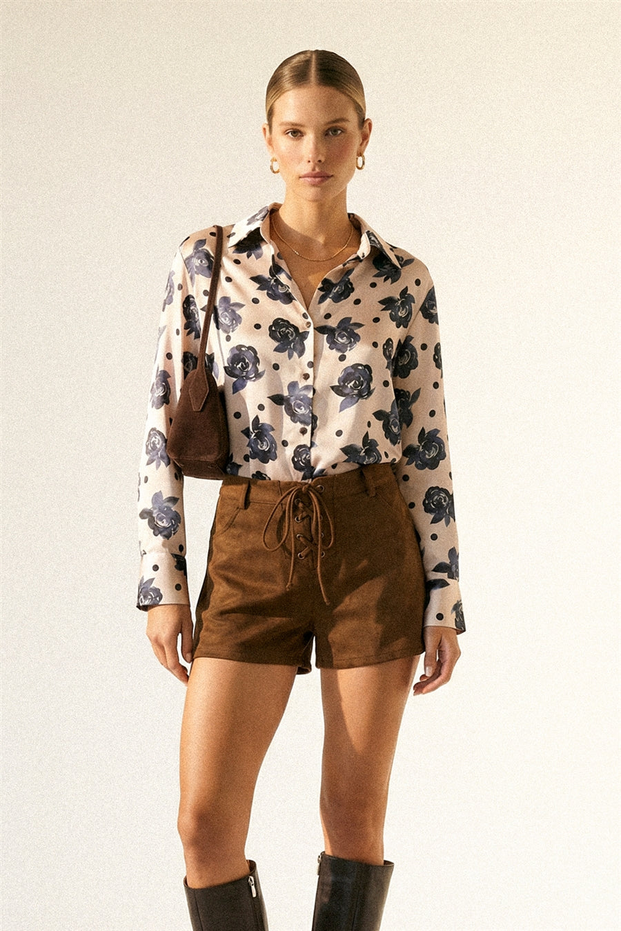 Woman wearing a floral blouse and brown shorts with a beige background