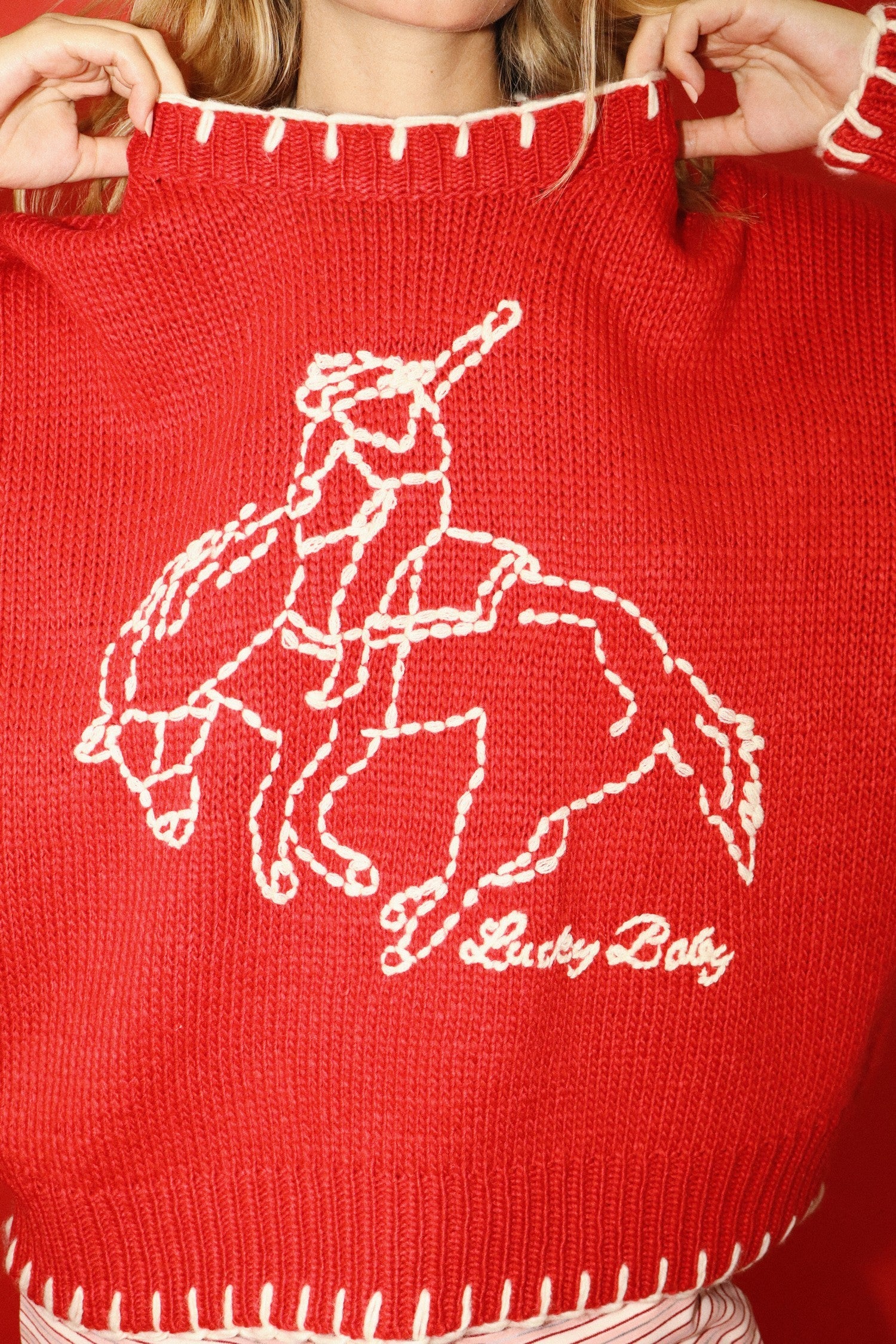Red sweater with white embroidered design of a person on a horse and 'Lucky Baby' text.