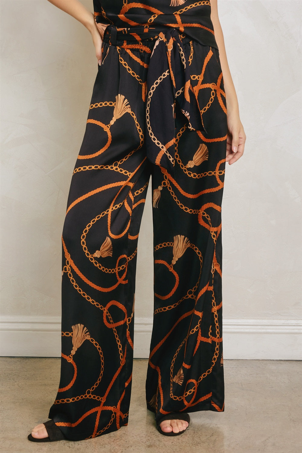 Black pants with orange chain pattern worn by a person on a plain background
