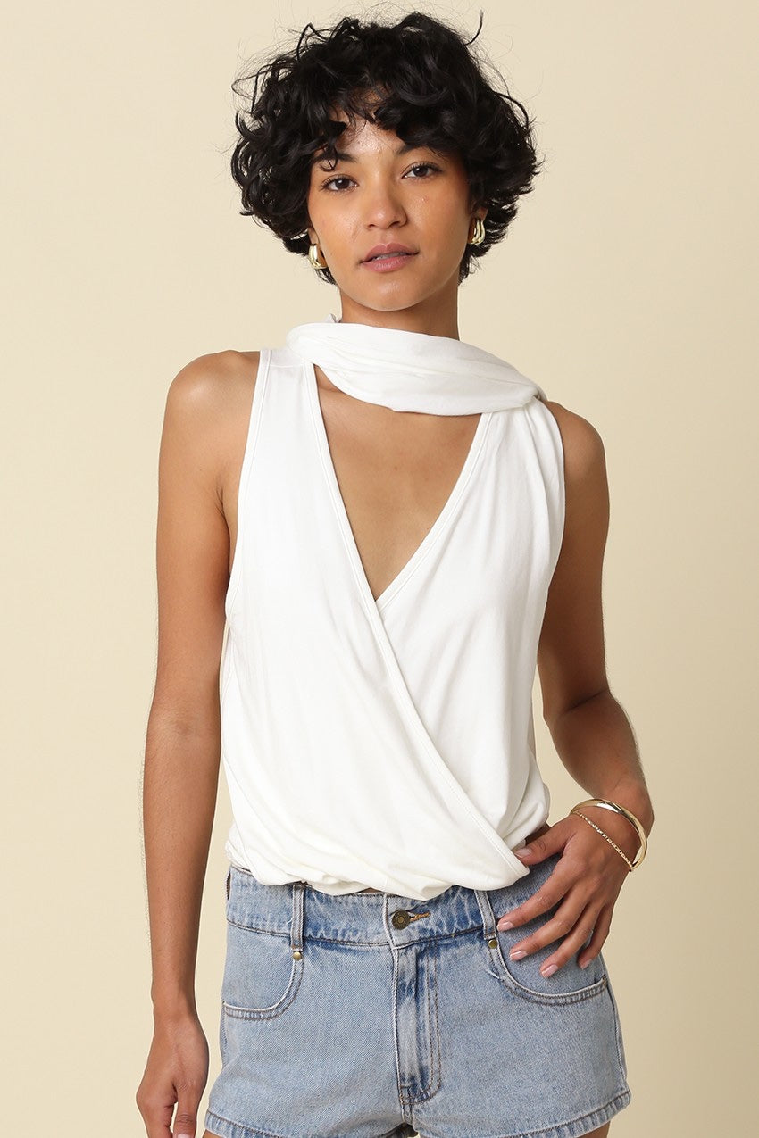 Woman wearing a white sleeveless top with a deep neckline and high-waisted blue jeans on a beige background