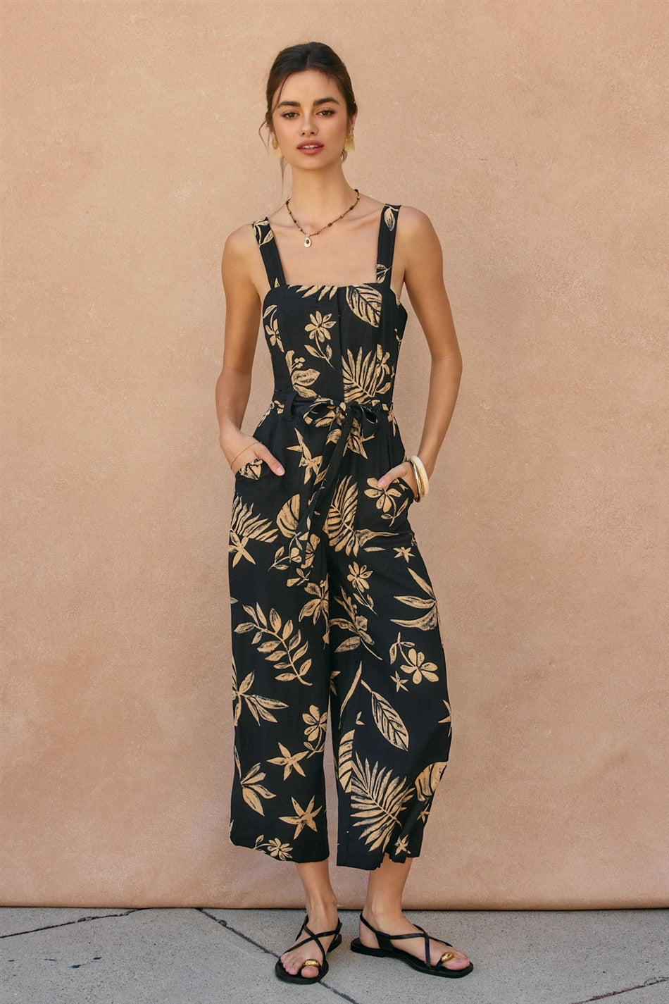 Woman wearing a black floral jumpsuit against a beige wall.