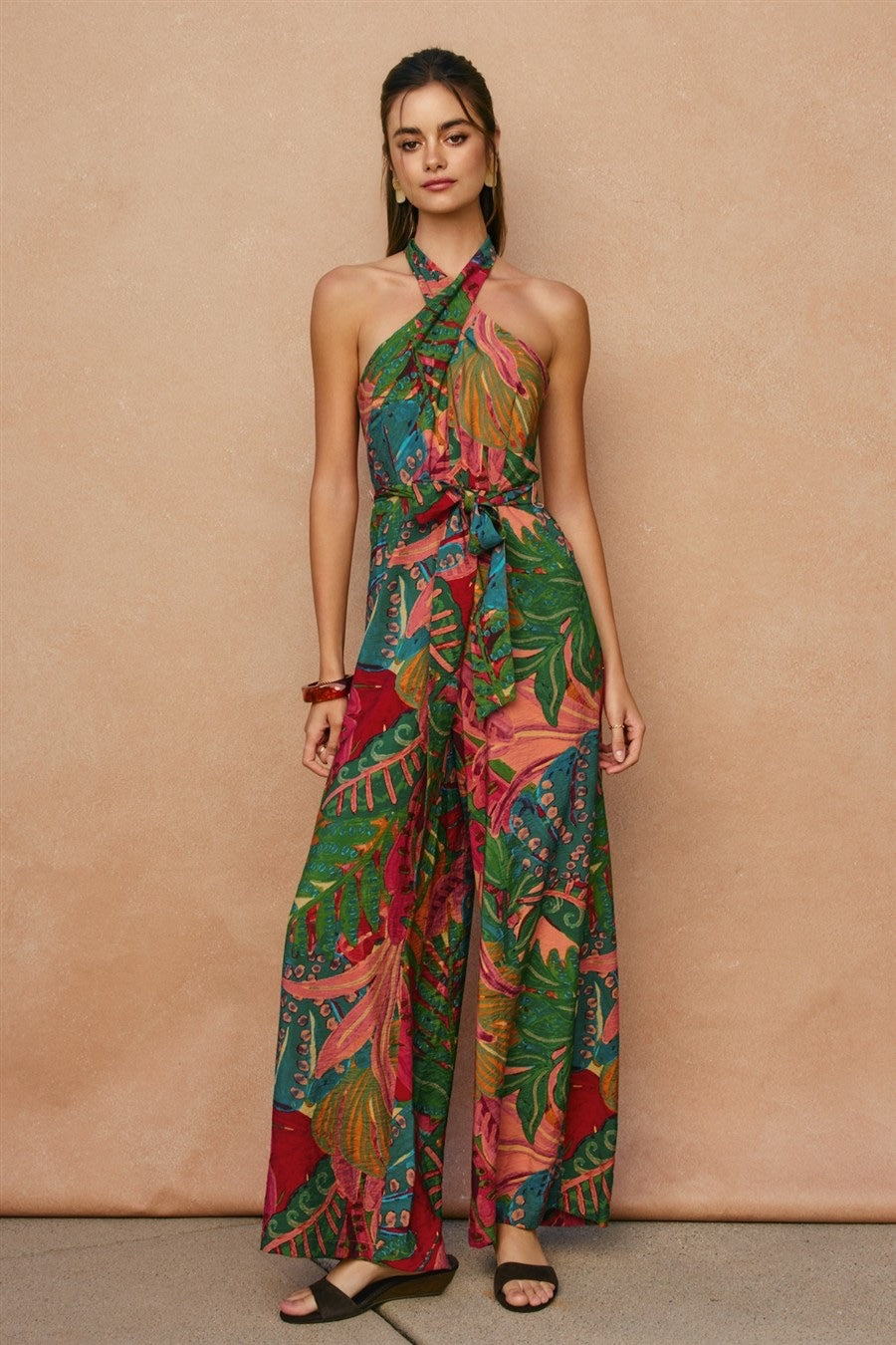 Woman wearing a colorful patterned jumpsuit against a beige background
Tropical print breezy rayon nylon wide leg jumpsuit.

- Crossed front halter neck with back tie closure
- Wide legs
- Sash belt
- Open back
- Smocked back panel with hidden center zipper closure
- Side pockets
- Lined