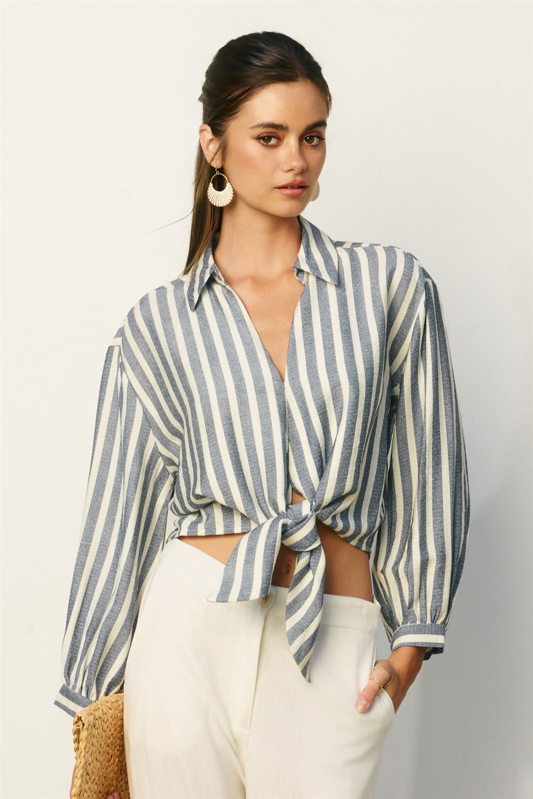 Woman wearing a striped shirt and white pants against a plain background