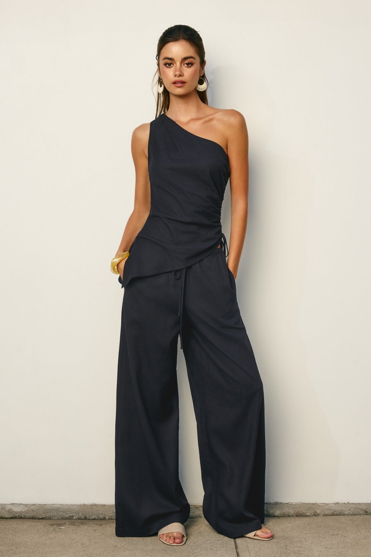 Woman wearing a NAVY one-shoulder jumpsuit against a plain background
