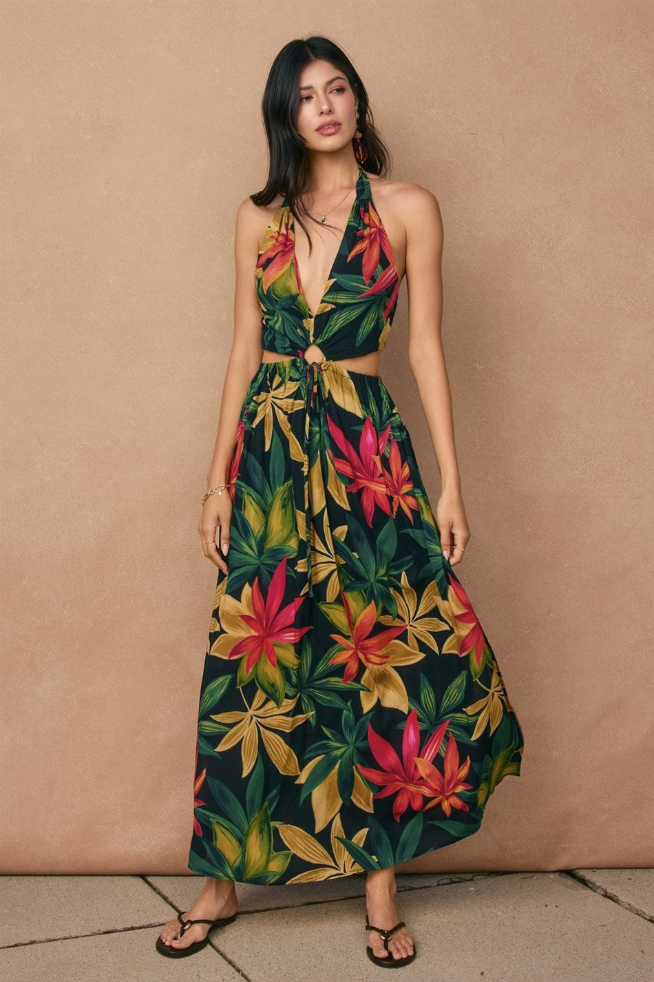 Woman wearing a floral dress against a beige background
Tropical printed halter neck maxi dress with an O ring and cutouts. 
- Halter neck tie closure
- Side and back cutouts 
- O ring and spaghetti sash tie closure at the waist
- Waist tie can be tied to the back
- Elastic waistband on the skirt
- Smocked back panel on the bodice
- Side slit
- Lined
